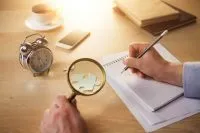 Writing hands with magnifying glass